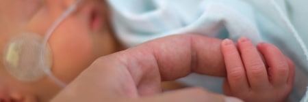 Adult holding baby's hand in hospital