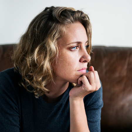 Woman sitting on sofa with head resting on hand