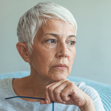 Portrait of a middle aged woman with head on hand and holding glasses