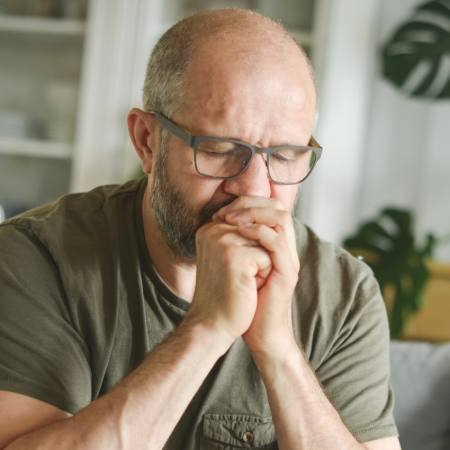 Man sitting at home looking pensive, with head in hands