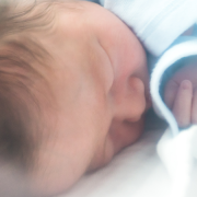 A baby in a blue sleep suit lies inside an incubator.