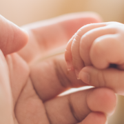 A baby's fist closed around the finger of an adult.