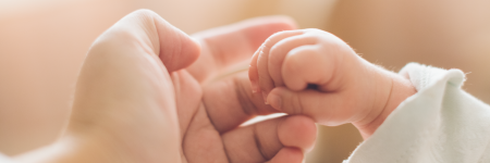 A baby's fist closed around the finger of an adult.