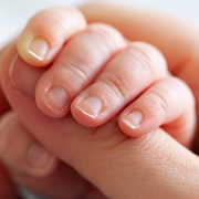 A close-up photo of a baby's hand wrapped around an adult's thumb