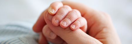 A close-up photo of a baby's hand wrapped around an adult's thumb